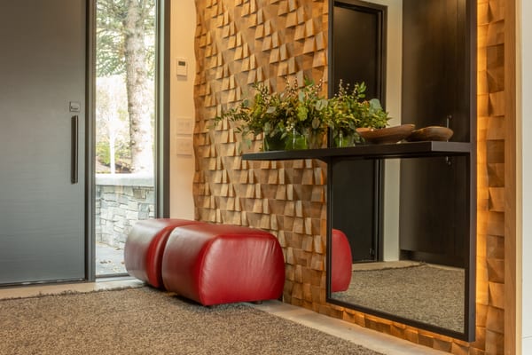 Entry with a carved wood feature wall, tall mirror and red leather ottoman