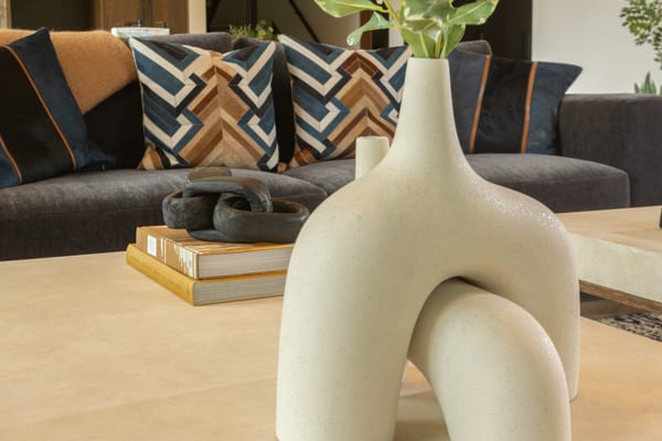 Sculptural cream vase on a stone coffee table in front of patterned pillows