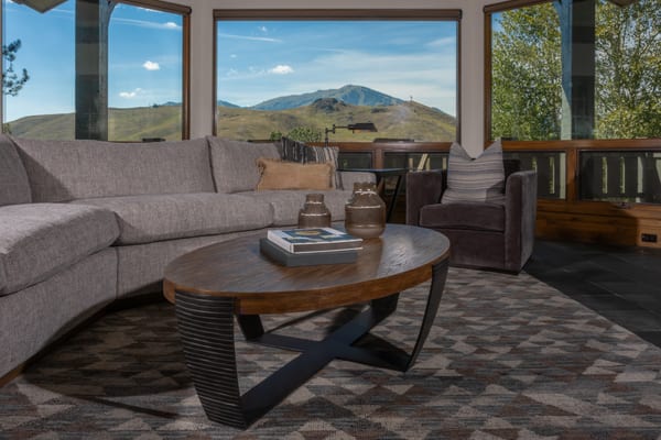 Curved sectional and oval coffee table facing a picture window with mountain views