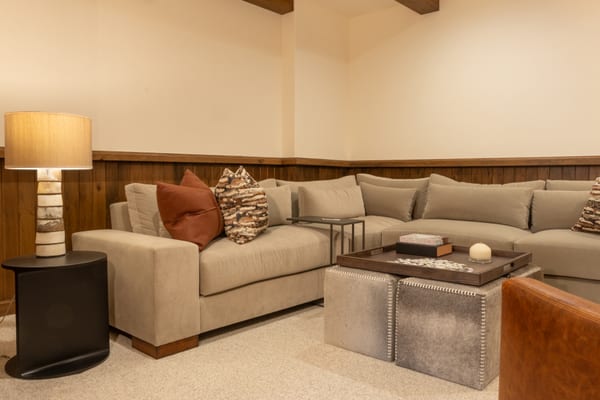 Family room with a taupe sectional, hide-covered ottomans and wood wainscoting