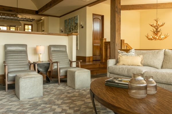 Great room with leather recliners, a linen sofa and an antler chandelier under timber beams