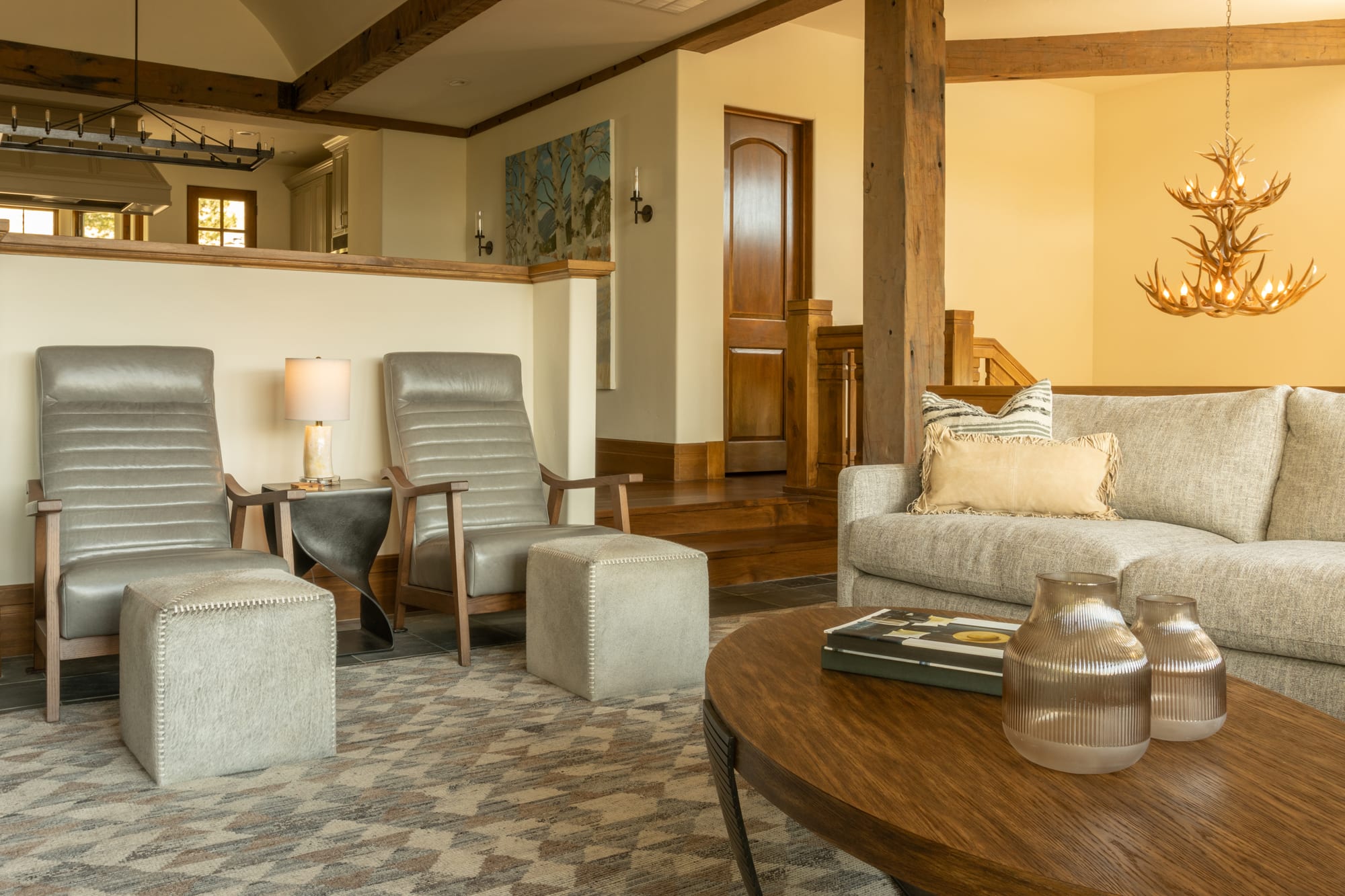 Great room with leather recliners, a linen sofa and an antler chandelier under timber beams