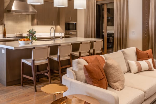 Kitchen island with leather counter stools, open to a cream sofa with rust pillows