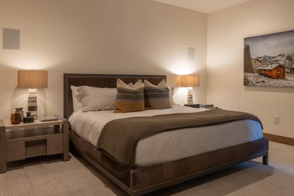 Bedroom with a suede bed, ribbed stone lamps and a painting of a mountain cabin