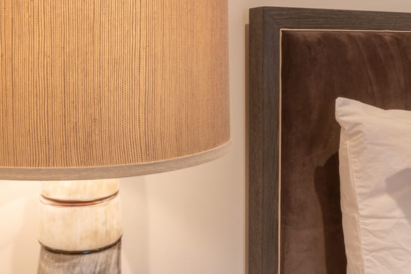 Close-up of a stone lamp base and linen shade beside a suede headboard