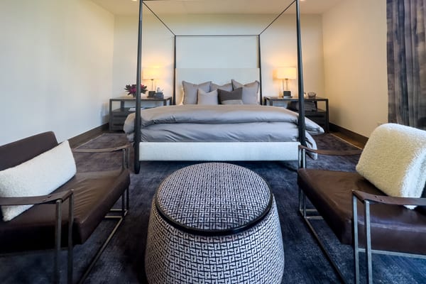 Bedroom with a black steel canopy bed, leather lounge chairs and a patterned ottoman