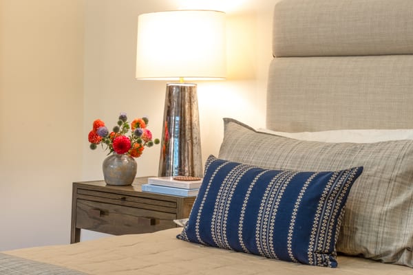 Bedside table with a mercury glass lamp and flowers beside a linen headboard