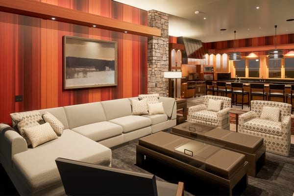 Rendering of a family room with a sectional and stone columns, open to the kitchen