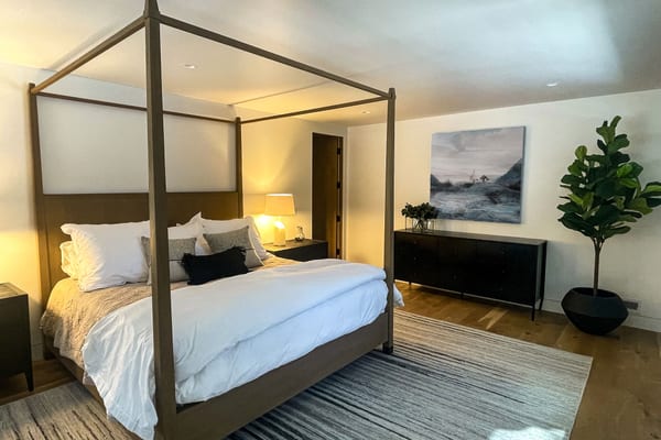 Bedroom with an oak four-poster bed, a black dresser and a striped rug