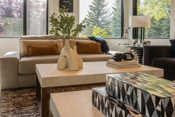 Cream sofa and stone-top coffee tables by tall windows looking out to the trees