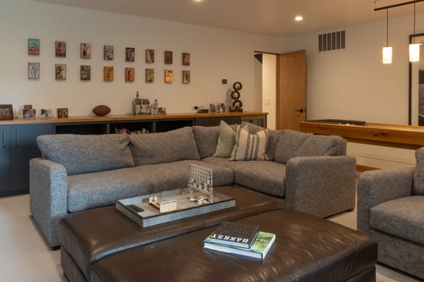 Family room with a grey sectional, a leather ottoman and a gallery wall of small artworks