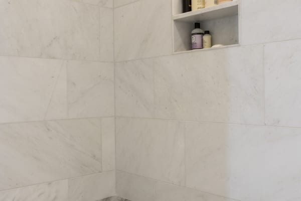 Marble shower with a lit niche and a grey stone bench