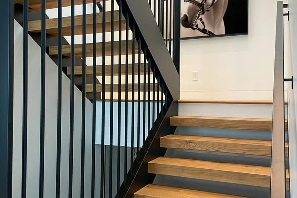 Open-tread oak staircase with black steel railings and a framed horse photograph