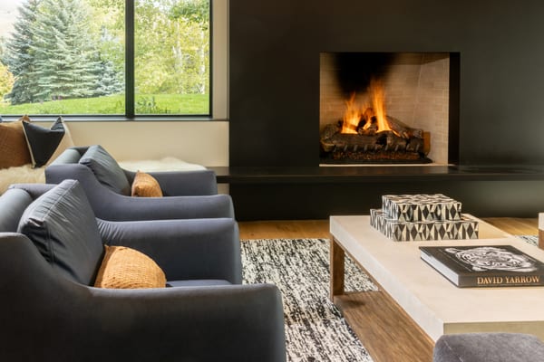 Lit fireplace in a black surround, with grey armchairs and a stone-top coffee table