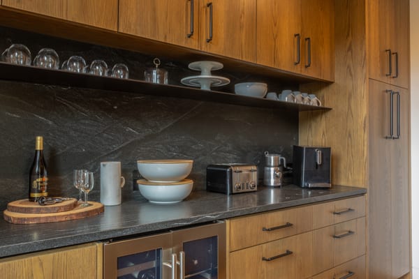 Coffee bar with oak cabinets, open shelves, a dark stone backsplash and a wine fridge