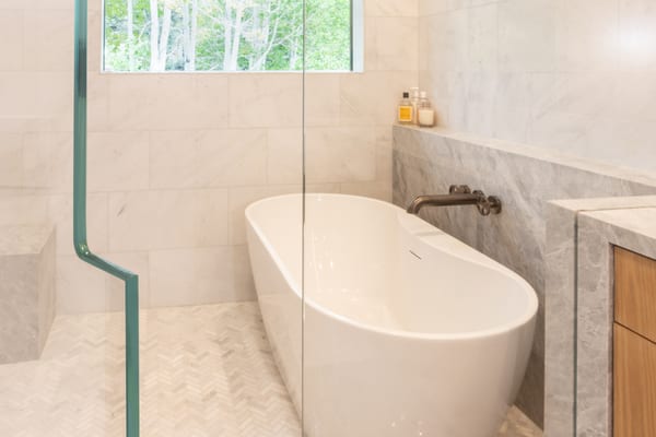 Freestanding tub against a grey marble ledge, behind a glass shower screen