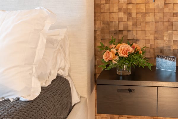 Nightstand with peach roses beside a white upholstered headboard