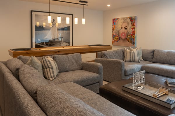 Family room sectional with pendant lights over a shuffleboard table and a pop art portrait