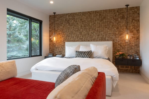 Bedroom with a wood block feature wall, glass pendant lights and a red daybed at the foot of the bed