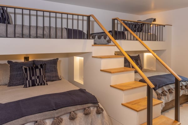 Bunk room with lit niches, navy blankets and oak stairs to the upper beds