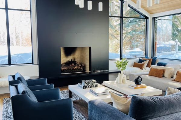 Living room with a black fireplace wall, ring chandelier and blue velvet seating under a wood ceiling
