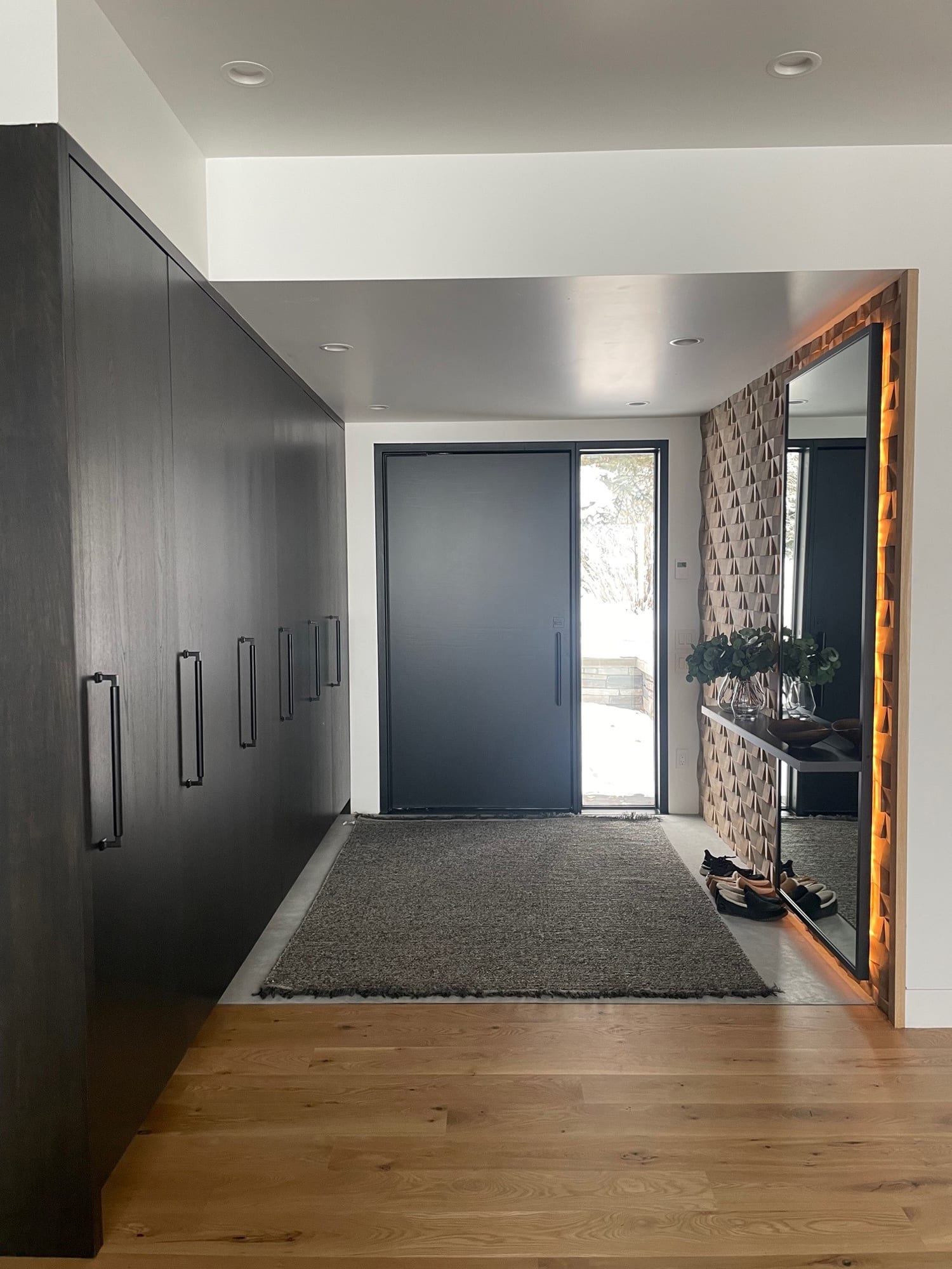 Entry hall with a wall of dark wood cabinets, a long runner and a lit mirror by the front door