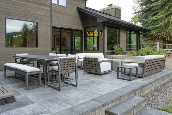 Stone patio with an outdoor dining table, lounge seating and a fire table behind the house