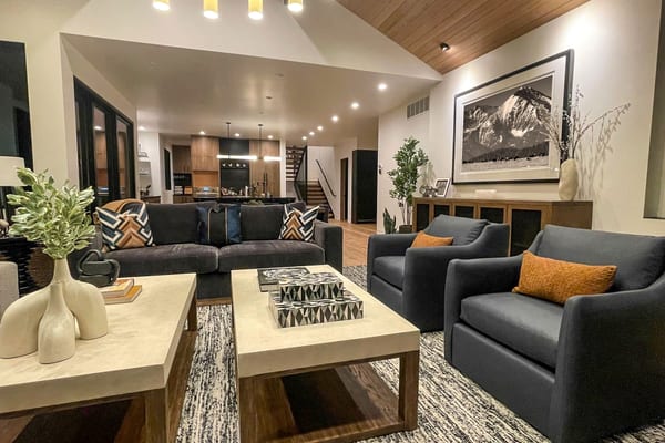 Living room with grey armchairs, stone-top coffee tables and a framed mountain photograph, open to the kitchen