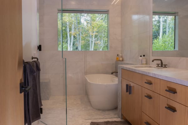 Main bathroom with a freestanding tub, marble walls, an oak vanity and a view of aspens