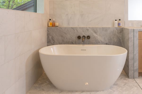 Freestanding tub with a wall-mounted bronze faucet and a grey marble surround