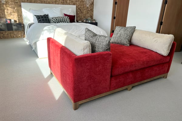 Red daybed with white and tweed pillows at the foot of the bed