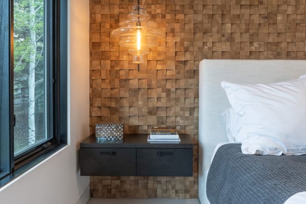 Floating nightstand under a glass pendant against a wood block wall