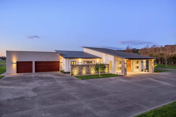 Front of the home at dusk, with a lit stone wall, covered entry and garage