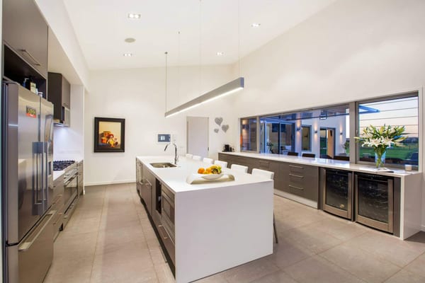 Kitchen with a white waterfall island, wine fridges and a counter along the windows
