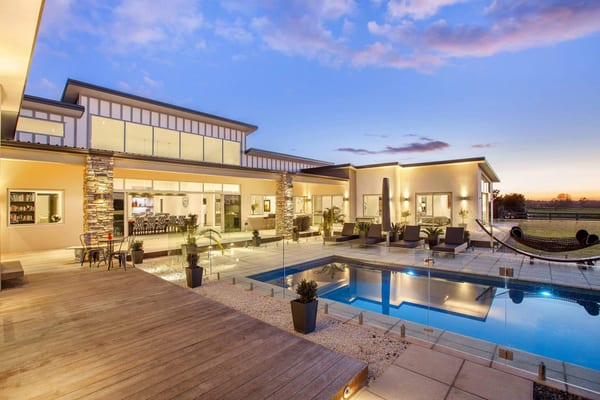 Pool, glass fence and timber deck at sunset, with stone columns framing the living area